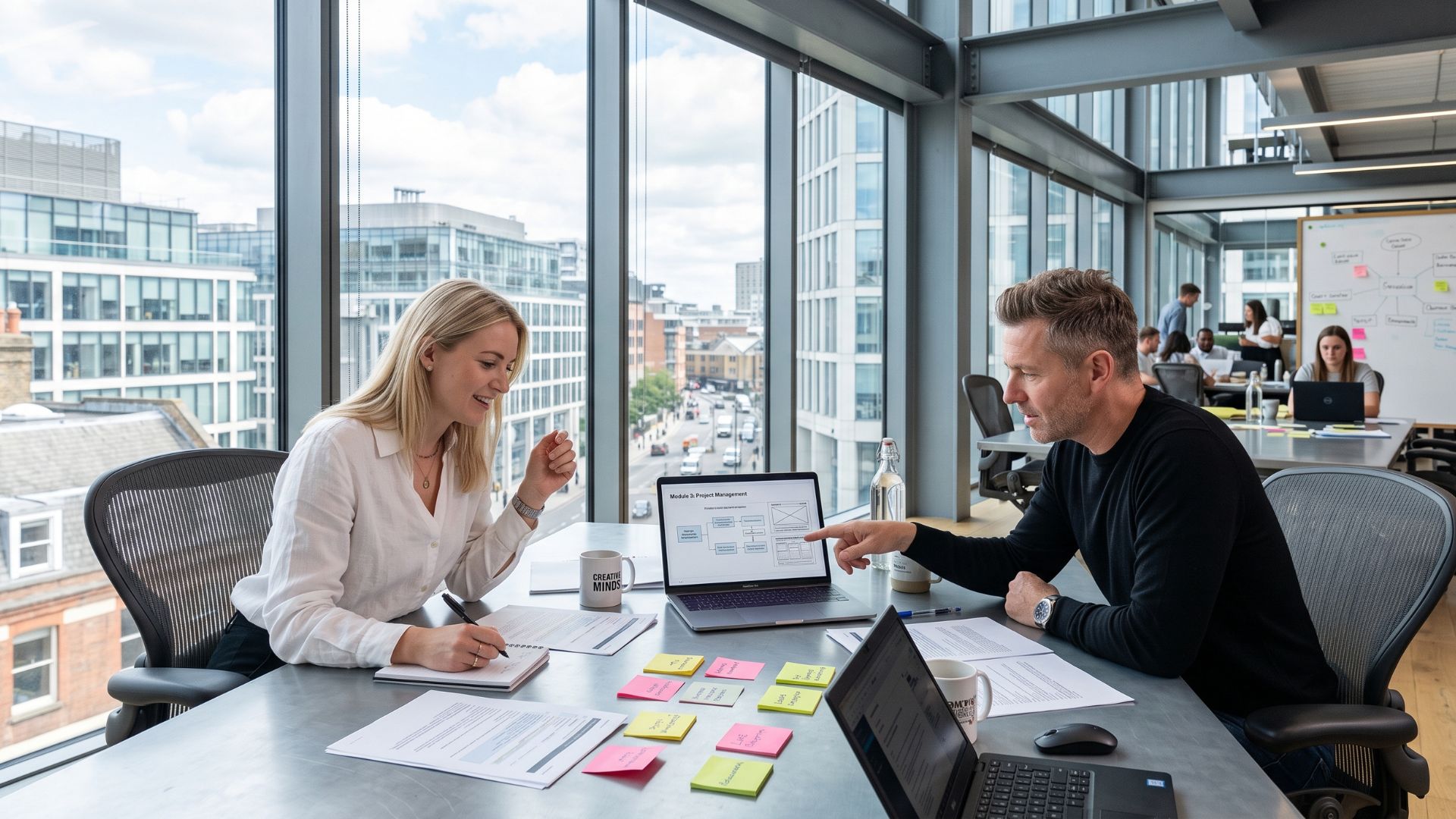 Two instructional designers reviewing a course storyboard on a laptop in a bright modern office with sticky notes and documents on the table